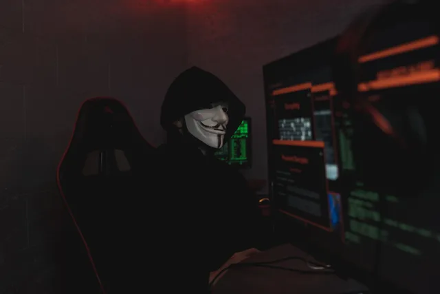An anonymous hacker wearing a mask working on a computer in a dark room. Impersonation policy template: what belongs in each section