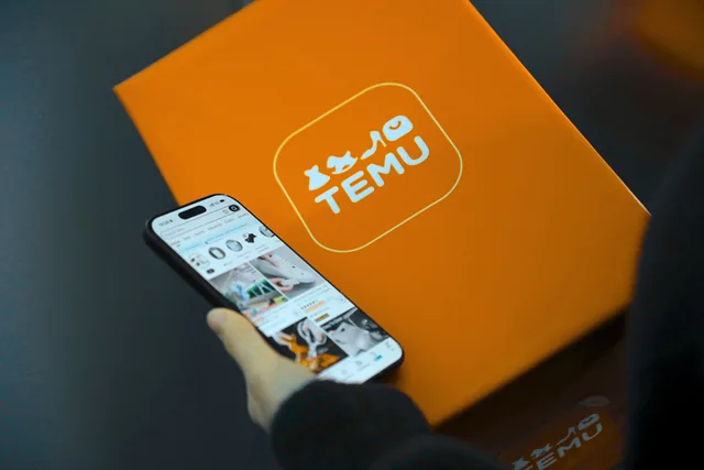 Hand holding smartphone with Temu app beside orange Temu package. Marketplace scams: keep deals on-platform