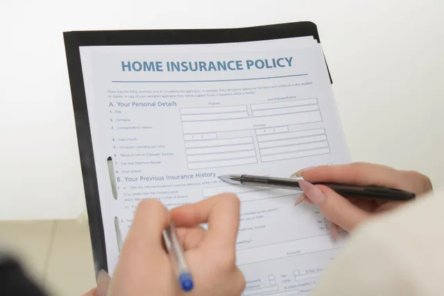 Hands holding pens filling out a home insurance policy document for coverage details. Marketplace scams policy template for small teams