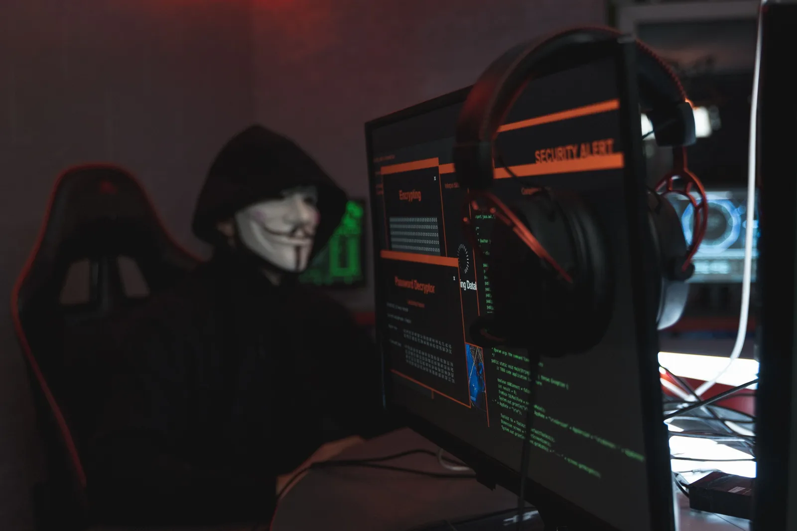 A person wearing a Guy Fawkes mask engaged in hacking activities on a computer in a dimly lit room. Phishing scams risks by disclosure and timeline